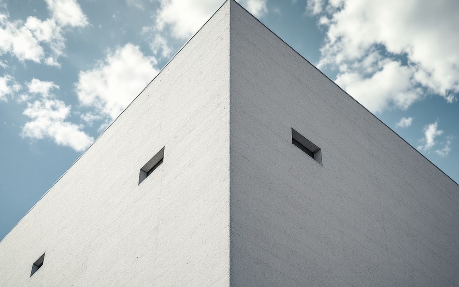 The corner of a large white-rendered building with strongly inward-sloping walls seen from below against the sky