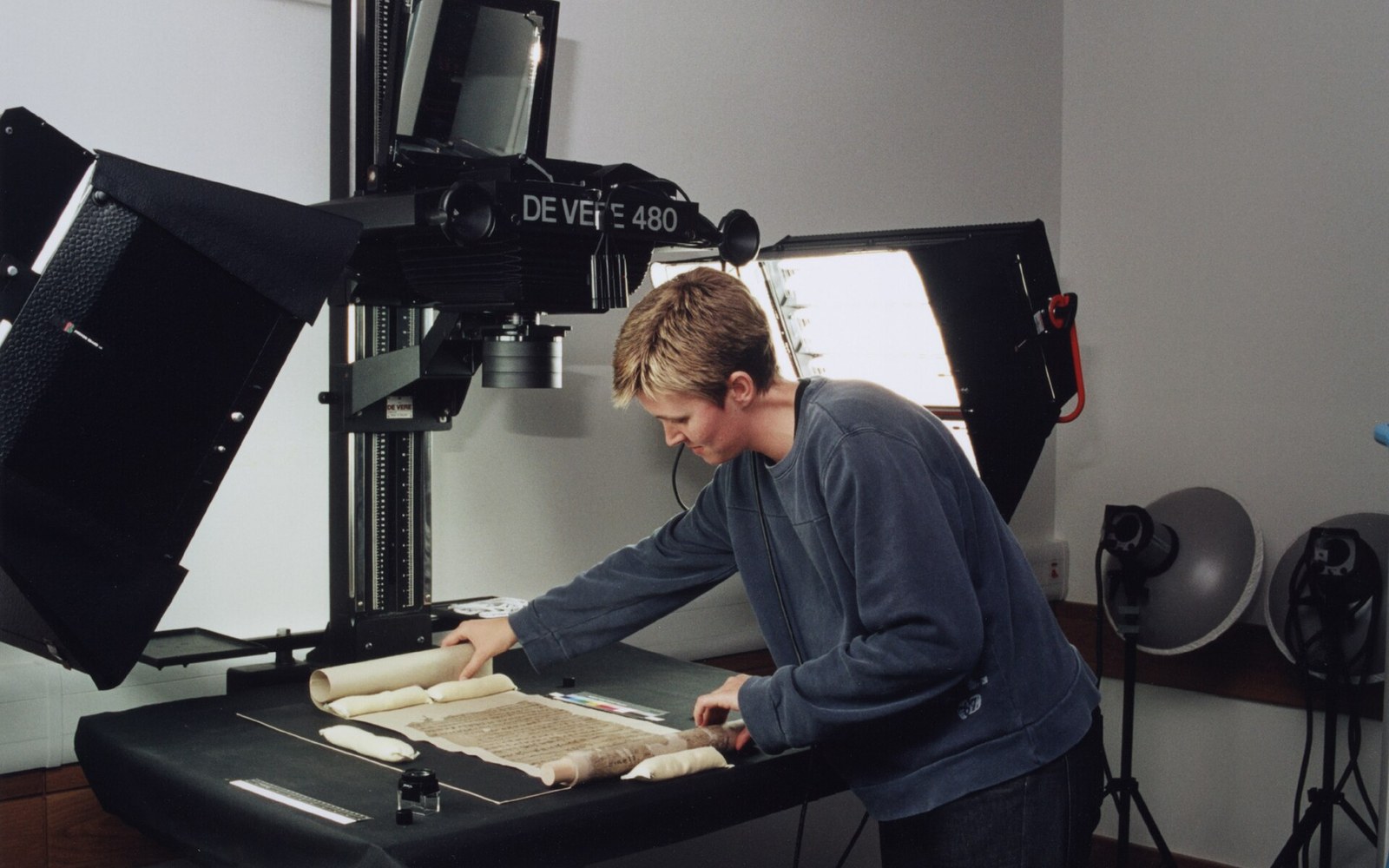 A technician photographs an unrolled ancient manuscript scroll using a large studio copy camera