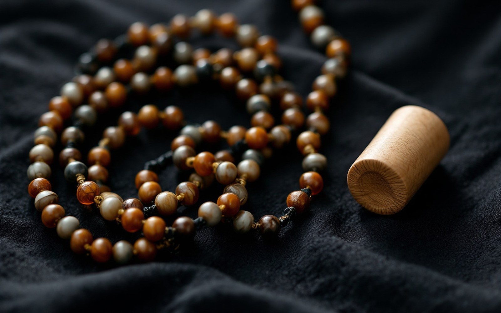 A hundred-bead rosary and a small hand-turned cylinder lying together on dark cloth, close, side light