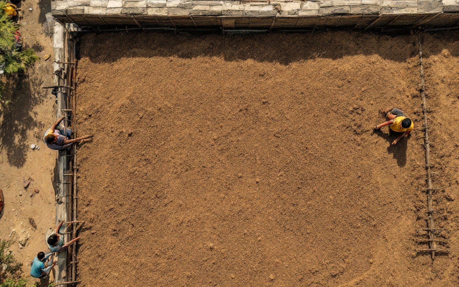 A flat roof of packed earth over closely spaced wooden poles seen from above, with a parapet at the edge